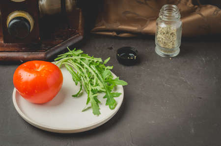 tomato and leaves of arugula in a white bowl with seasonings against a dark background. Top viewの写真素材