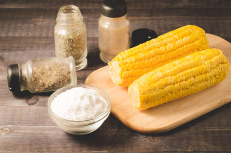 boiled corn with salt and seasonings on a wooden tableの写真素材
