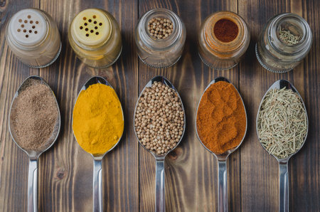 Set of various aromatic colorful spices in spoons and in glass jars on a wooden table. Top view