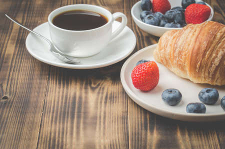 Delicious breakfast with cup of coffee and croissant with fresh berries. Wooden table. の写真素材