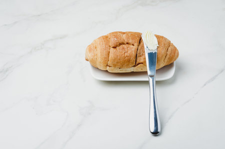 Croissant and a knife with butter on a white stone table. French breakfast