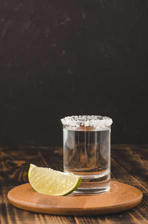 Tequila shot and lime slice on wooden table/Tequila shot and lime slice on wooden table. Dark background.の写真素材