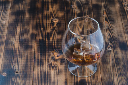 Glass of cognac with ice cubes on a wooden table/Glass of cognac with ice cubes on a wooden bar,...