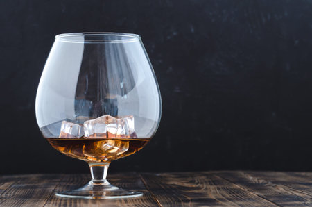 Glass of cognac with ice cubes on a wooden bar/Glass of cognac with ice cubes on a wooden bar. Black...