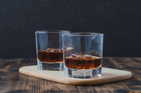 Two Glasses of whiskey with ice cubes on a wooden table/Two Glasses of whiskey with ice cubes on a wooden table. Black background with copyspace.の写真素材