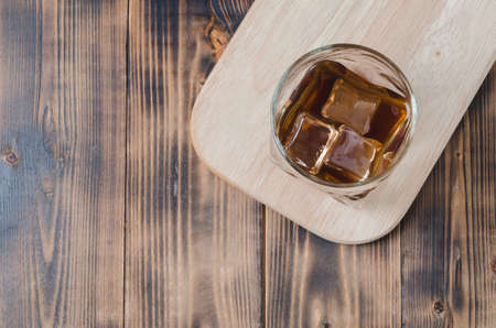 Glass of cognac with ice cubes on a wooden table/Glass of cognac with ice cubes on a wooden table. Top view, copyspaceの写真素材