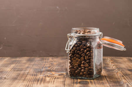 Coffee in a glass jar on a wooden table. Selective focus. Coffee grains in an open glass jar on a wooden table and background for text.の写真素材