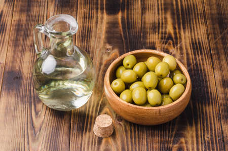 Olive oil bottle and olives on wooden background. Top view. Olive oil in a bottle and fruits of olives in a wooden bowl.の写真素材