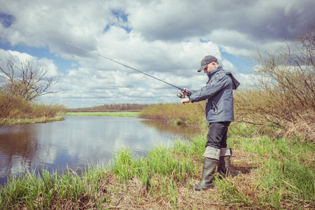 Fisherman throws spinning rod on the river bank. Autumn fishing.