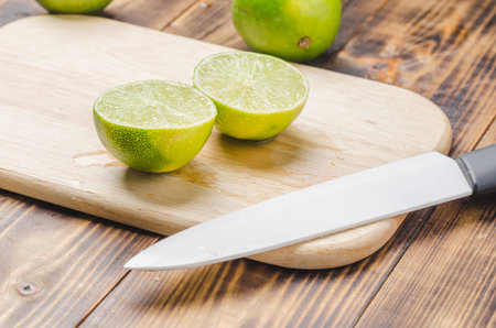Sliced â€‹â€‹limes with a white bladed knife on a wooden board.