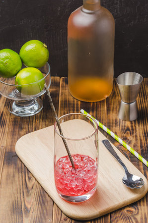 red cocktail with making tools and limes on wooden table. Selective focus.