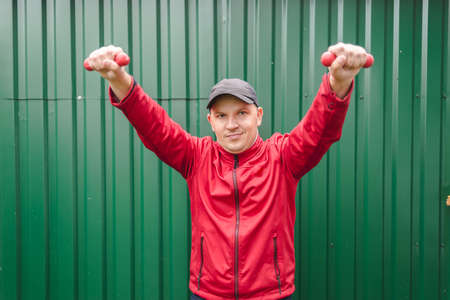 Guy in a red tracksuit is boxing with dumbbells on a green background.の写真素材