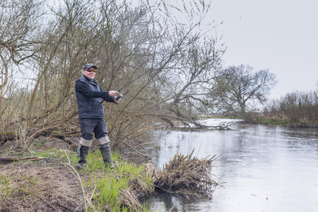 Fisherman pulls a fish with a spinning rod standing on the river. Male hobby.