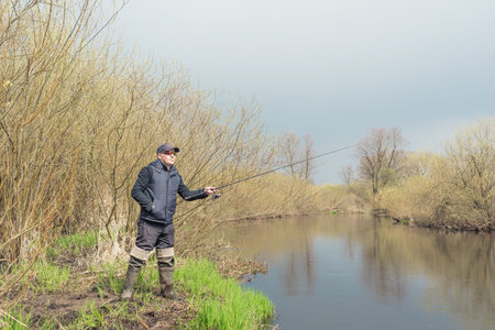 Man fishing on the bank of the river in the rain.