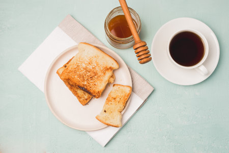Toasts on a plate, a spoon on a jar of honey and coffee in a cup. Breakfast still life. top view.の写真素材