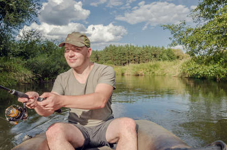 Fisherman sits in a boat in his hand with a spinning rod. Happy angler on a sunny summer day.の写真素材