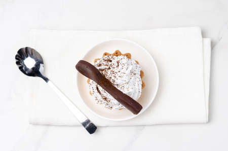 Cake basket with protein white cream decorated with a chocolate spoon on the white in a white plate on a napkin. top view.の写真素材
