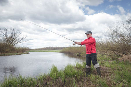 Fisherman in a red jacket is fishing on the green bank of the river. beautiful sceneryの写真素材