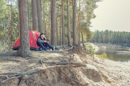 Young man near the tent with a camera photographs a beautiful landscape.の写真素材