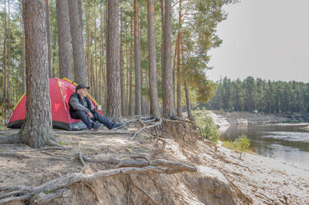 Young man sits near a tent in the forest in the rock. Camping.の写真素材