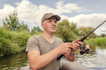 Portrait of a young man in a boat with a spinning rod. Sunny day.の写真素材
