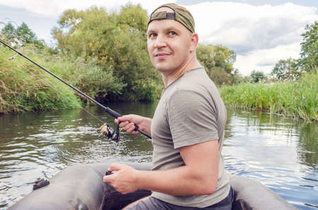 Fisherman sits in a boat in his hand with a spinning rod. Happy angler on a sunny summer day.の写真素材