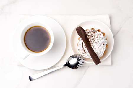 Cake basket with protein white cream decorated with a chocolate spoon in a white plate on a napkin and a cup of coffee. Dessert theme. top view.の写真素材