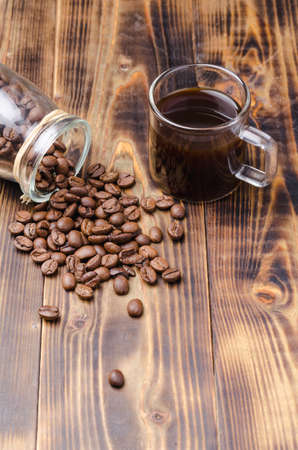 Cup of coffee and beans are scattered from a glass jar on a wooden table. top view.の写真素材