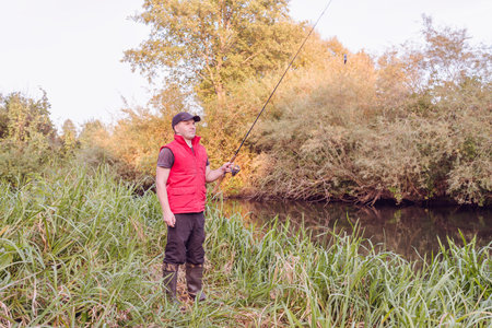 Fisherman in a red vest with a fishing rod on the shore. hobby.の写真素材