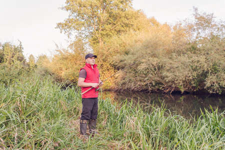 Fisherman in a red vest with a fishing rod on the shore. hobby.の写真素材