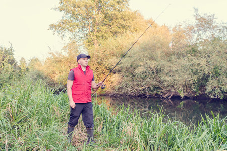Fisherman in a red vest with a fishing rod on the shore. hobby.の写真素材