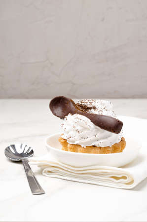 Cake basket with protein white cream decorated with a chocolate spoon on the white in a white plate on a napkin.の写真素材