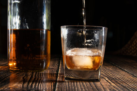 Glass of whiskey with ice cubes, a bottle on a wooden table. An old tabletop with light and a glass...