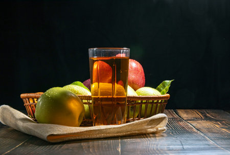 Apples in a basket on a wooden table on a black background, a glass of apple juice.の写真素材