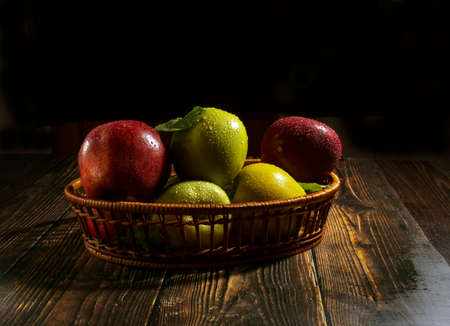 A basket of fresh apples in dew drops on a wooden table on a dark background.の写真素材