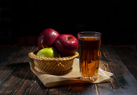 Apples in a basket on a wooden table on a black background, a glass of apple juice.の写真素材