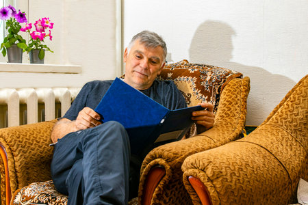 A man reads the latest news or documents, checking documents or bills, Happy man using a laptop, making documents or communicating while sitting on an armchair in the living roomの写真素材