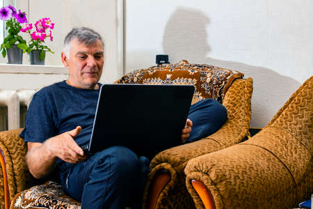 A man sitting in a chair with a computer remotely writing an email or reading the news. A man attends distance education courses, plans work, or communicates online.の写真素材