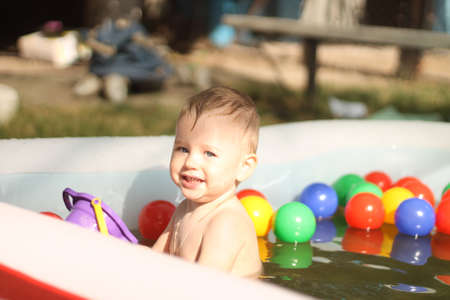 Laughing boy in the children's pool. Sunny summer mood picture. A cheerful kid plays in the pool with drops of water under bright sunshine.の写真素材