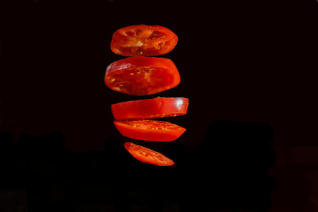 Sliced â€‹â€‹tomato on slices on a black background. Flying slices of tomato.