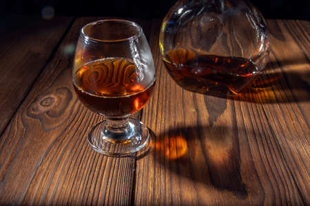 Pour cognac or brandy into a large glass on an old rustic table. Vintage wood background, night mood. Place for text, dark background, selective focus.の写真素材