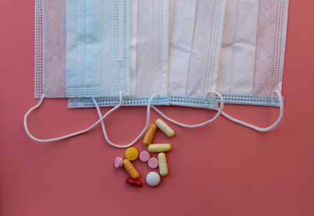 medical mask and pills, pills scattered on pink background close-up with copy space
