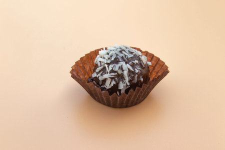 Coconut petit four is a juicy chocolate sponge cake with coconut filling and topping with coconut flakes. Mini cake on a beige background. Selective focus. Place for text.の写真素材