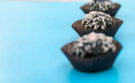 Coconut petit four is a juicy chocolate sponge cake with coconut filling and topping with coconut flakes. Mini cake on a blue background. Selective focus. Place for text.の写真素材