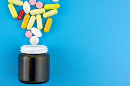 Multicolored pills and capsules, pill bottle, pharmaceutical medicine pills on a turquoise...