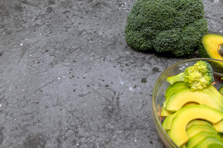 Avocado salad with broccoli, cucumber and lettuce in a bowl on a dark concrete background. View from...