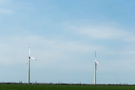 Group of low angle view of wind turbine towers again cloudy blue sky at the wind farm. Green,...