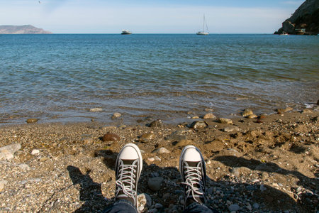 Legs of a man in sneakers relaxing on a sandy beach, casual young man in sneakers sitting on the...