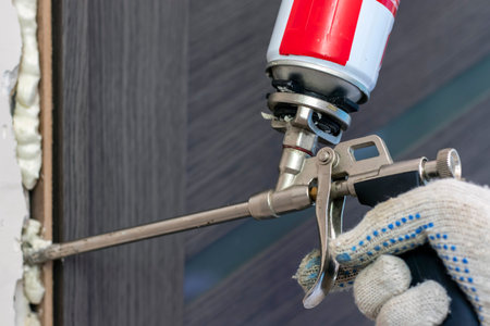 A man's hand uses a spray bottle to fill the gap with construction foam between the new wooden door and the wall. Close-up. Renovation work at home.の写真素材