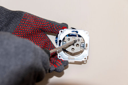 An electrician uses a screwdriver to plug the power cord into an outlet.